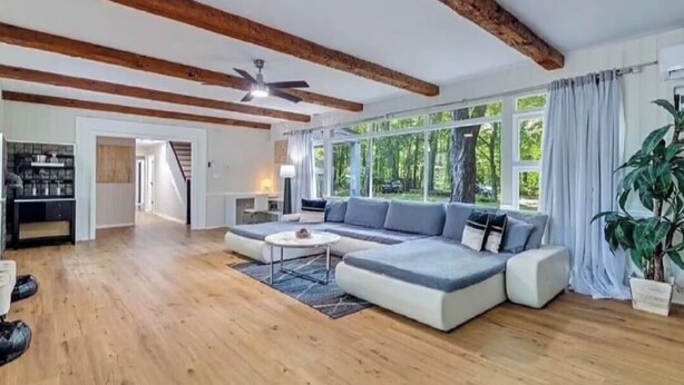Un ampio soggiorno con un grande divano componibile, travi in legno a soffitto e ampie finestre.
