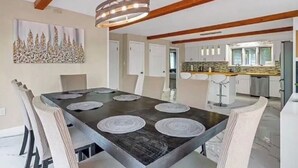 Zona pranzo con tavolo in legno scuro, sedie bianche e lampadario a sospensione.
