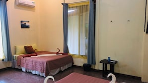 A hotel room with two beds, a window with curtains, an air conditioner, and a small table.
