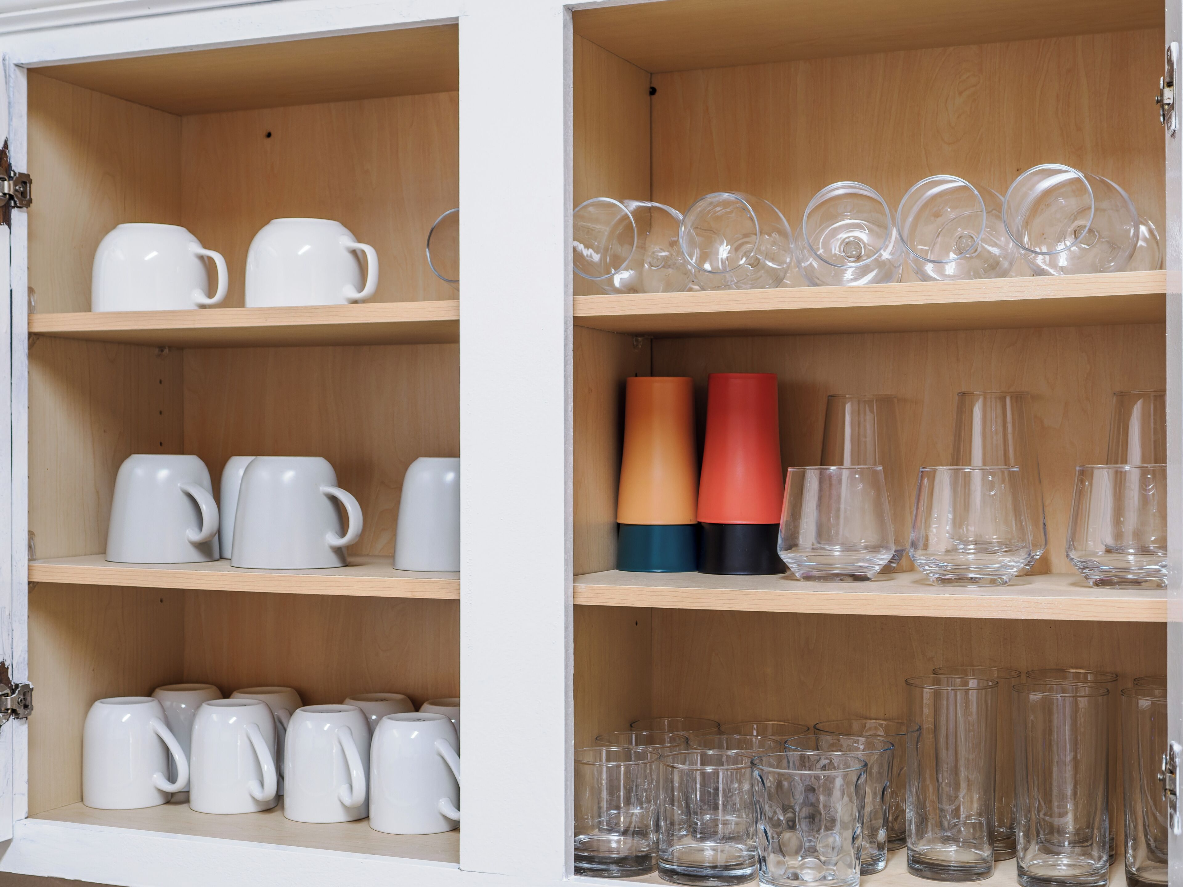 A cabinet with shelves containing white mugs, clear drinking glasses, and colorful vases.