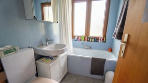 Ein Badezimmer mit Toilette, Waschbecken, Badewanne und Fenster mit Pflegeprodukten.