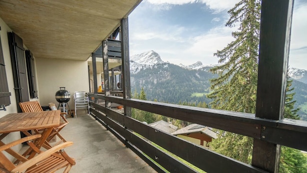 Ein Balkon mit Blick auf schneebedeckte Berge, einem Holztisch und einem Grill.