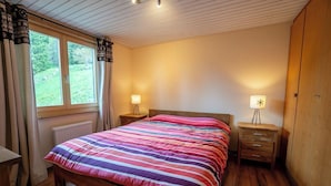 Ein Schlafzimmer mit einem hölzernen Bett, zwei Nachttischen mit Lampen, einem Fenster mit Vorhängen und einer Heizung.