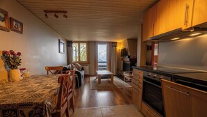 Eine Küche mit Holzausstattung, einem Esstisch mit gemustertem Tischläufer und Blick ins Freie durch ein Fenster.