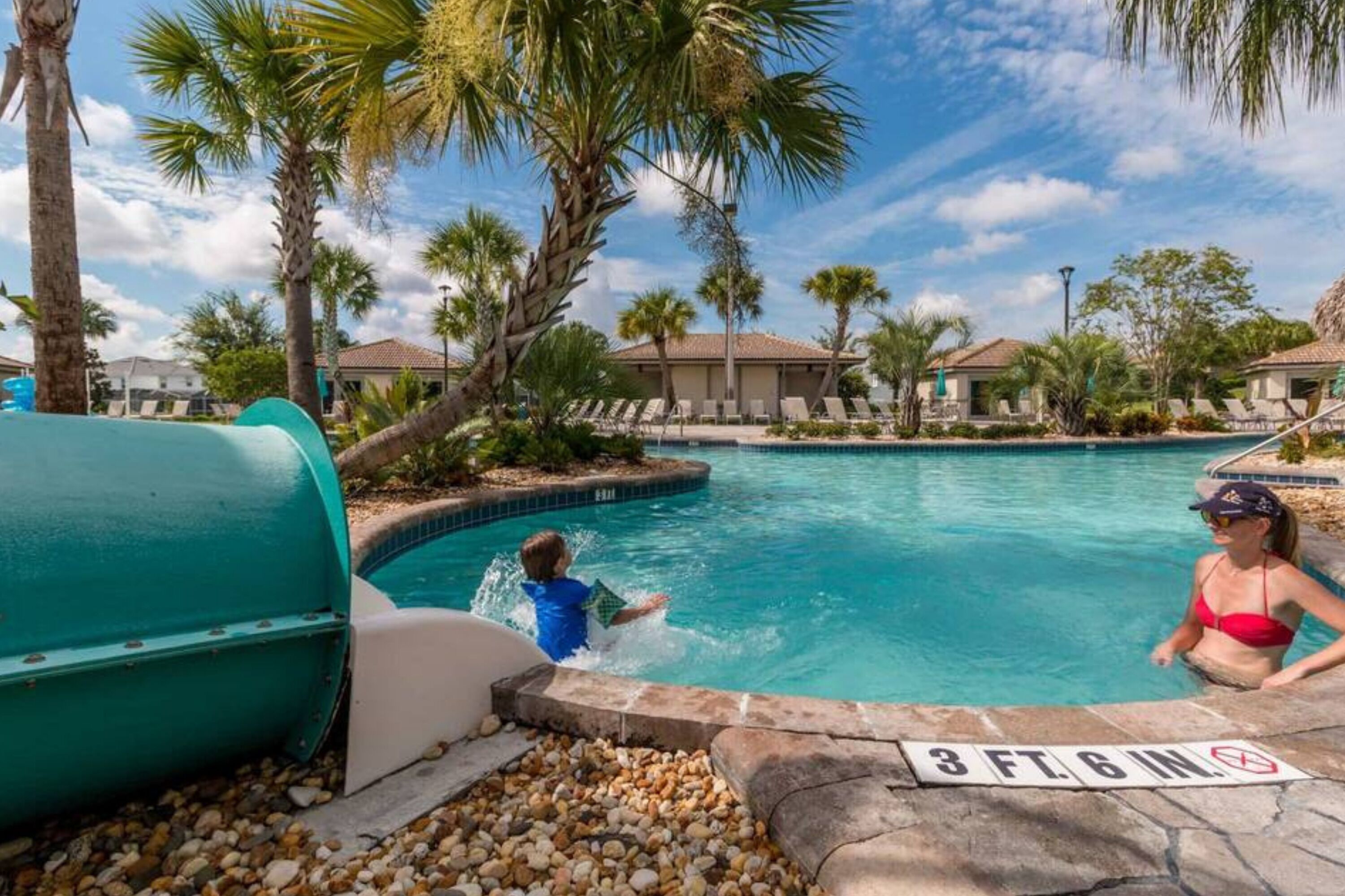A swimming pool with a 3 ft. 6 in. depth sign, surrounded by palm trees and lounge chairs.
