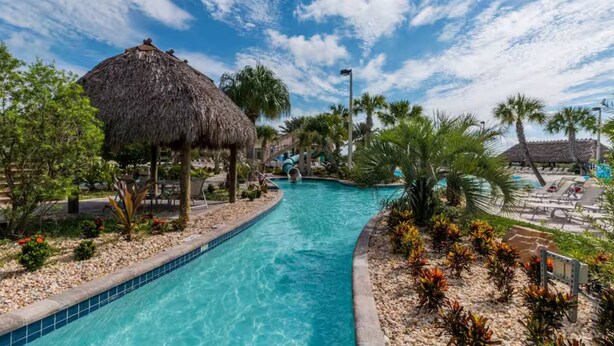 A swimming pool with a slide, surrounded by palm trees and a thatched-roof structure. - Private Pool 4BR Getaway in ChampionsGate (Four corners)