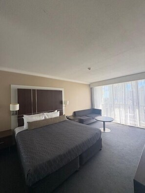 A hotel room with a large bed, a sofa, a small table, and a large window with curtains. - View - 1627 (1BR/1BA) (Gold Coast)