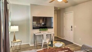 A living room with a ceiling fan, a flat-screen TV mounted on the wall, a small white table with a plant, a round coffee table, and a sofa. - West Plains 2BR Near Downtown Pet Friendly Stay (West Plains)