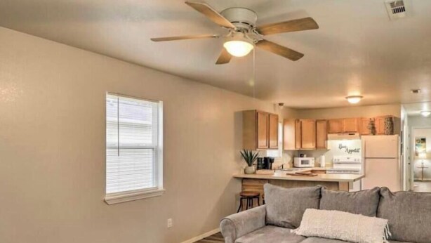 A living room with a ceiling fan, a couch, and a kitchen area in the background. - West Plains 2BR Near Downtown Pet Friendly Stay (West Plains)