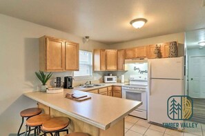 A kitchen with wooden cabinets, a central island with stools, a microwave, a stove, and a refrigerator.
