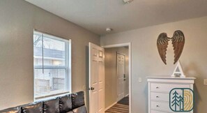 A hallway with a door, a window with blinds, a white dresser with a logo, and a brown leather couch.