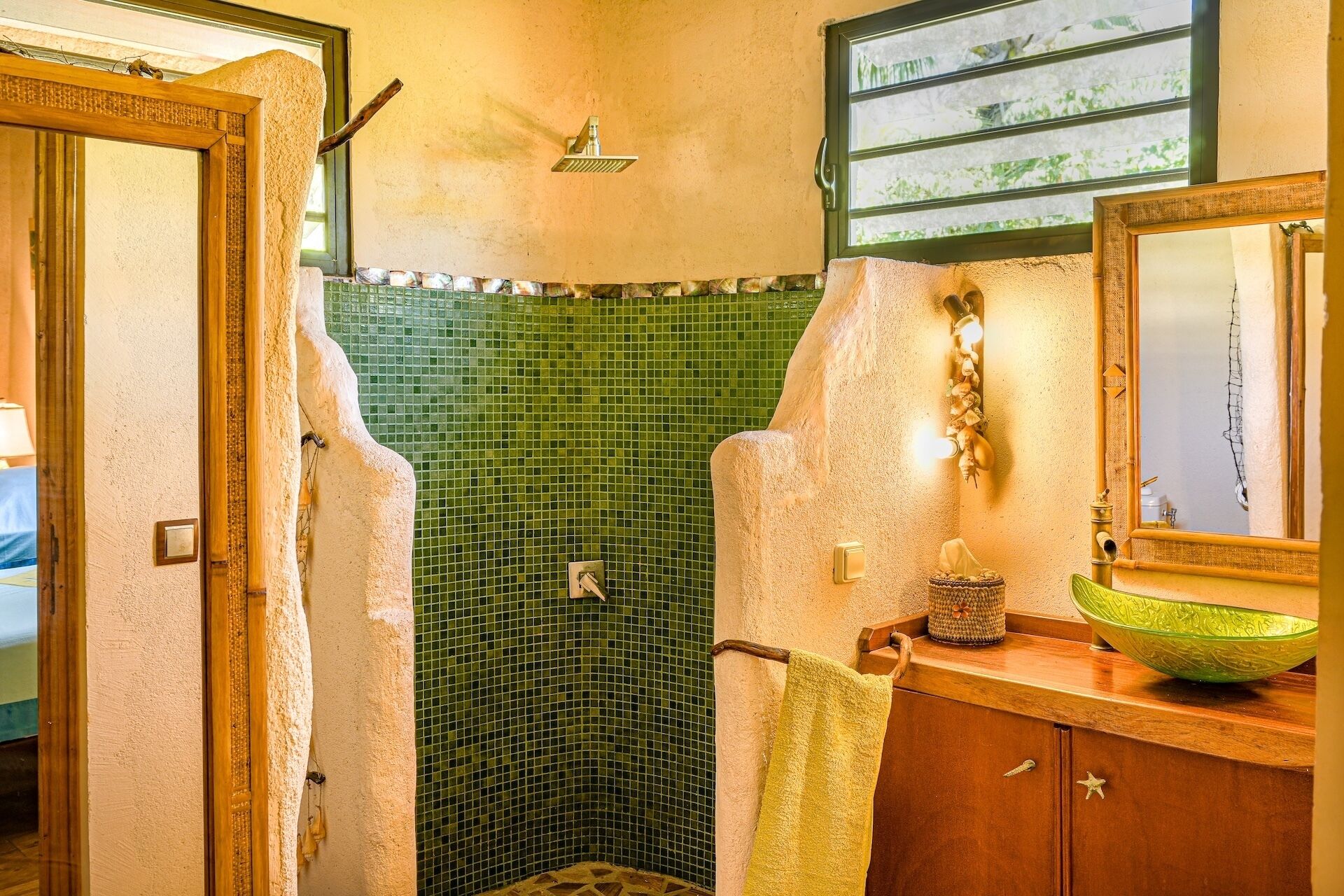 A bathroom with a green mosaic wall, a wooden vanity with a green bowl, and a mirror.