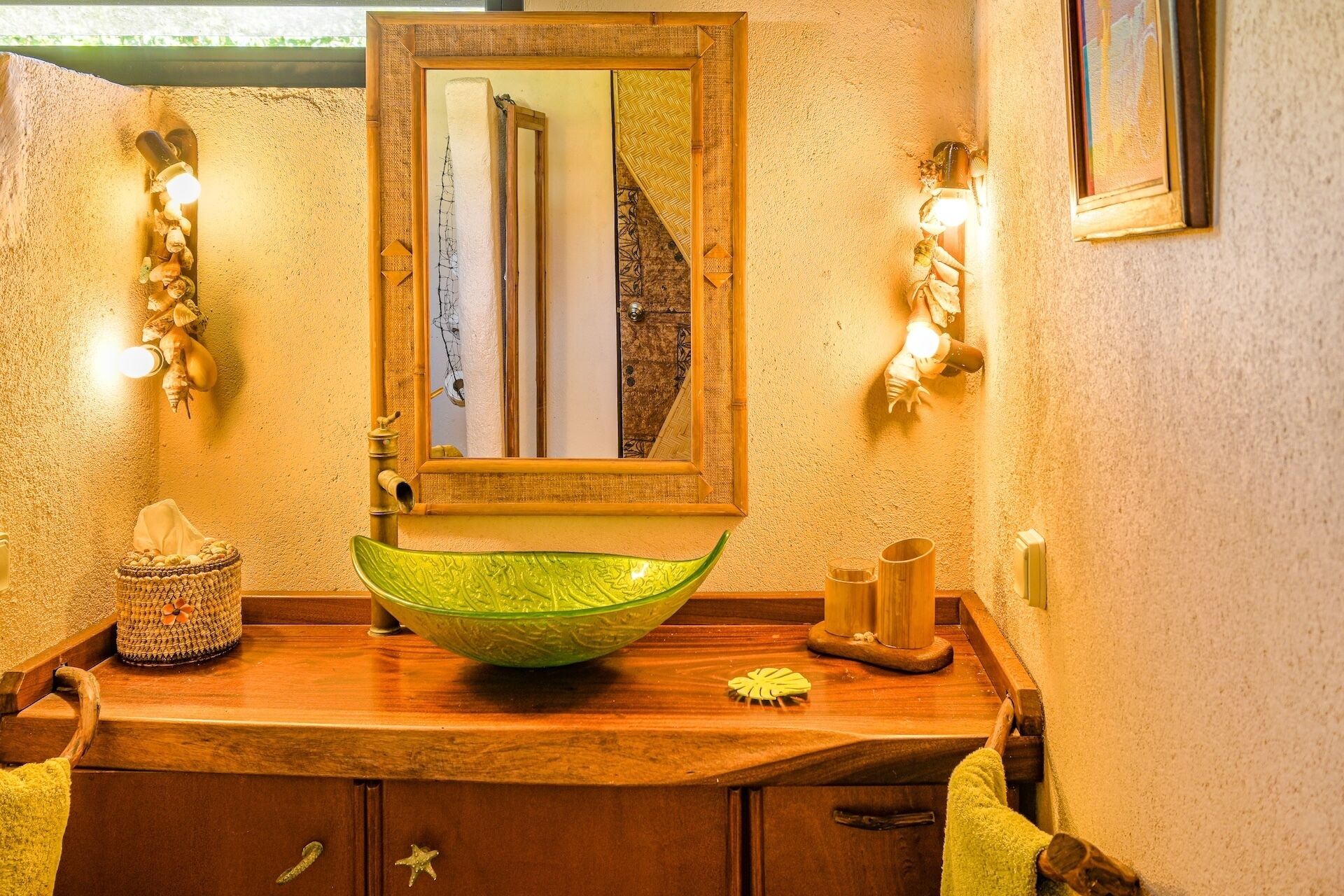 A bathroom with a wooden vanity, a green glass bowl sink, a mirror, and wall-mounted lights.