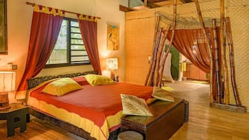 A room with a bed, a nightstand, a lamp, a window with curtains, and a woven bamboo structure.