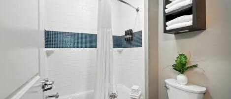 A bathroom with a bathtub, toilet, and a shelf with towels.