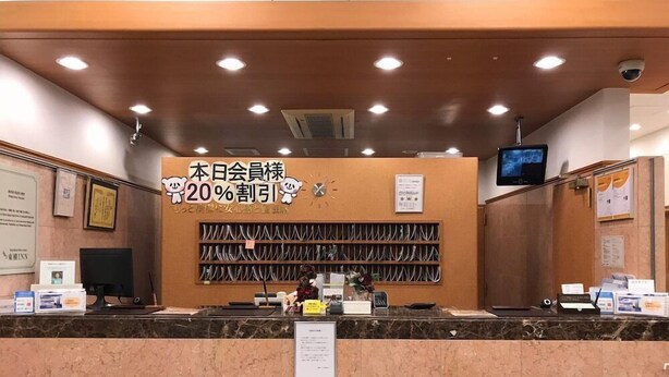 Un comptoir d’accueil d’hôtel avec un panneau indiquant une réduction de 20 %, un ordinateur et un téléviseur fixé au mur.
