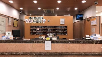 A hotel reception desk with a 20% discount sign, a computer, and a TV mounted on the wall.