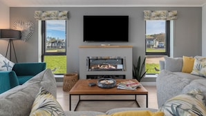 A modern living room with a fireplace, a flat-screen TV, and a view of the outdoors. - Bryn Hafod - Luxury Lodge, Hot Tub, Walk to Beach (Penally)