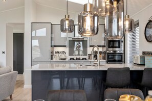 Une cuisine moderne dotée d’un îlot central, d’appareils électroménagers en acier inoxydable et de luminaires suspendus.