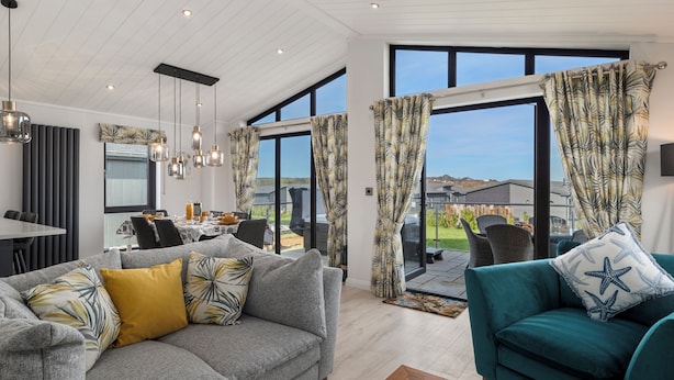 A modern living room with a grey sofa, teal armchair, and a dining area with a table and chairs. - Bryn Hafod - Luxury Lodge, Hot Tub, Walk to Beach (Penally)