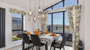 A dining area with a table set for four, large windows, and hanging pendant lights. - Bryn Hafod - Luxury Lodge, Hot Tub, Walk to Beach (Penally)