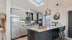A modern kitchen with a skylight, a central island, and bar stools. - Bryn Hafod - Luxury Lodge, Hot Tub, Walk to Beach (Penally)
