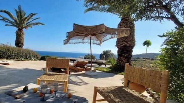 Un espace extérieur aménagé avec du mobilier en bois, une table avec des boissons et un grand parasol pour faire de l’ombre.
