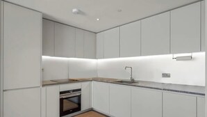 A modern kitchen with white cabinetry, a built-in oven, and a granite countertop. - ✨ River View Apartment Near O2 | Sleeps 6 | Prime Location London ✨ (london)