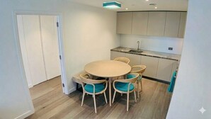 A compact kitchen with a round table and chairs, a built-in sink, and light-colored cabinets. - ✨ River View Apartment Near O2 | Sleeps 6 | Prime Location London ✨ (london)