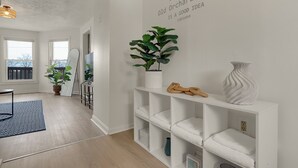 Un salón moderno con una pared blanca, una planta en maceta, un estante blanco con toallas y una alfombra azul.