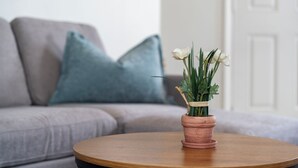 Una mesa redonda de madera con una maceta de terracota que contiene flores blancas y follaje verde.