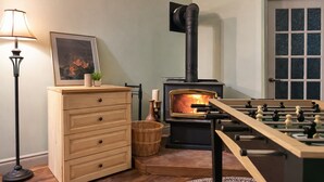 A cozy room with a wood-burning stove, a wooden dresser, a lamp, and a foosball table. - 51 Acre Summer Farmhouse-Hottub, Stargazing, BBQ-Sleeps upto 8 (Colborne)