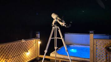A telescope on a tripod on a wooden deck with a hot tub in the background.