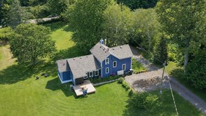 A two-story house with a large front porch, a garage, and a well-maintained lawn. - 51 Acre Summer Farmhouse-Hottub, Stargazing, BBQ-Sleeps upto 8 (Colborne)