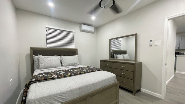 Een slaapkamer met een bed, een dressoir, een plafondventilator en een raam met jaloezieën.
