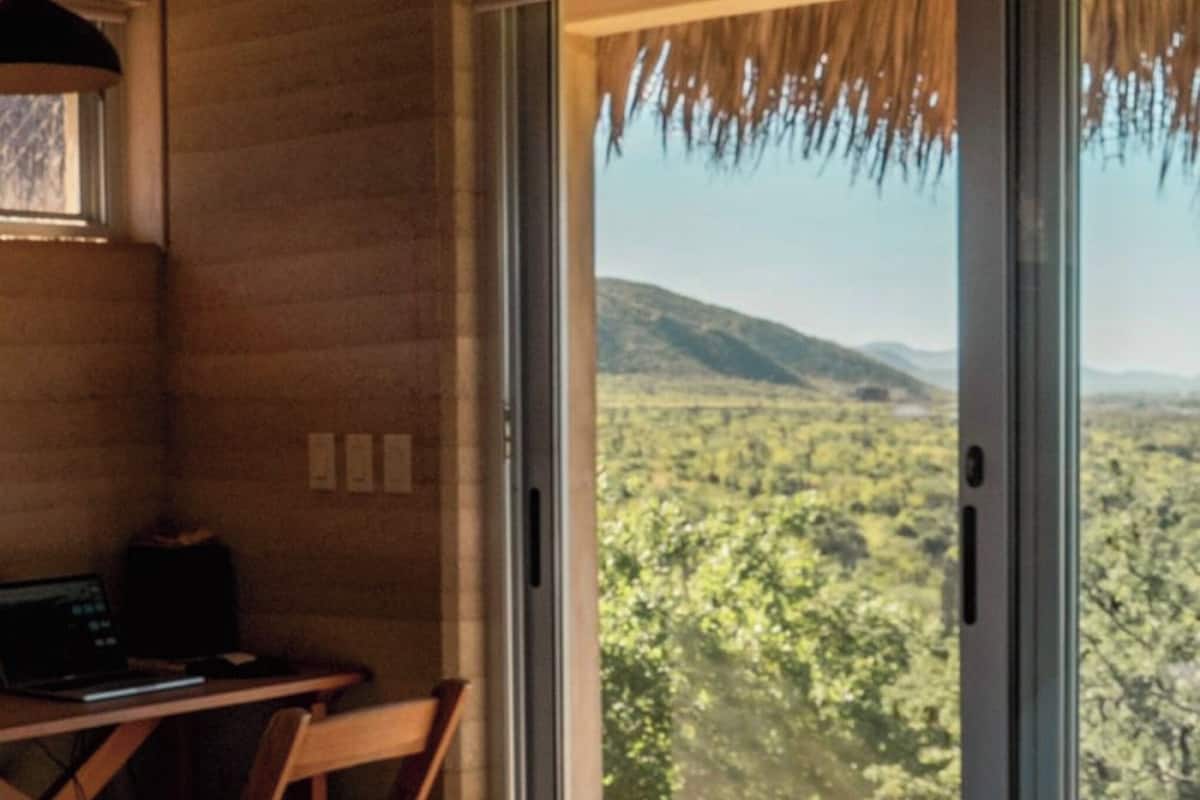 A bedroom with a large bed, a desk, and a view of a mountainous landscape through a sliding glass door.