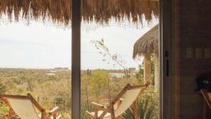 A room with a large sliding glass door leading to an outdoor deck with two wooden chairs. - Hotel Cabanas uno (El Pescadero)