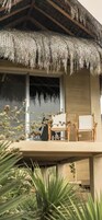 Un edificio con techo de paja, un balcón con sillas y una ventana con vistas a árboles.
