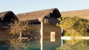 A clear swimming pool with a wooden structure and thatched roofs in the background. - Hotel Cabanas uno (El Pescadero)