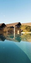 Una piscina cristalina con una estructura de madera y techos de paja al fondo.