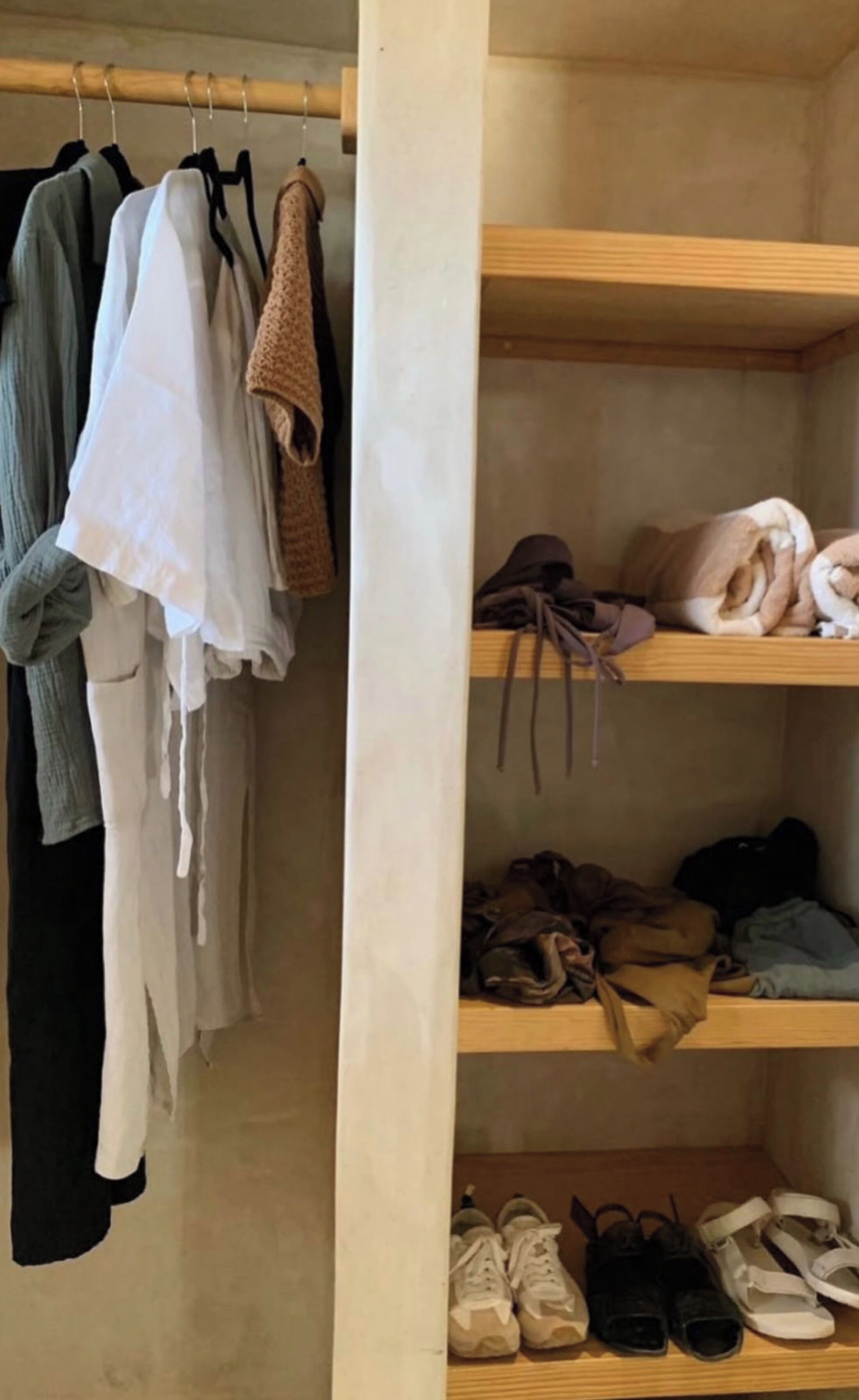 A closet with hanging clothes and shelves containing folded clothes and shoes.