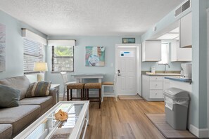 A compact living space with a sofa, a dining table with chairs, a kitchen area with cabinets, and a trash bin. - (Saint Pete Beach)
