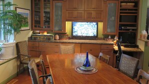 Una cocina con muebles de madera, una mesa de comedor, sillas, un televisor y una planta en maceta.