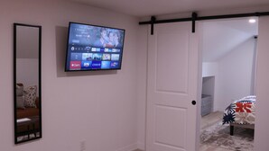 A bedroom with a TV mounted on the wall, a sliding door, a bed with a patterned bedspread, and a small bedside table.