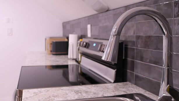 A modern kitchen with a stainless steel sink, a black countertop, and a tiled backsplash.
