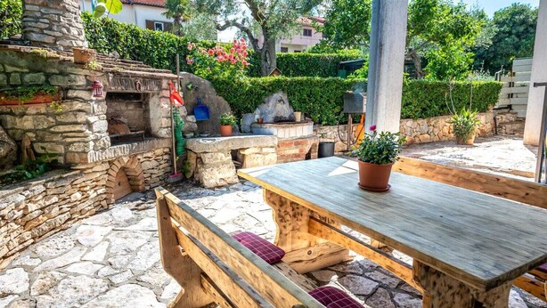 An outdoor patio with stone flooring, a wooden table, benches, and a stone oven. - Apartment 2425/200961 (Istria - Rovinj), 1300m from the beach (Rovinj)