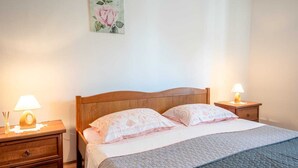 A bedroom with a wooden headboard, two bedside tables with lamps, a bed with patterned bedding, and a wall-mounted painting of a rose. - Apartment 2425/200961 (Istria - Rovinj), 1300m from the beach (Rovinj)