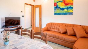 A living room with a sofa, a television on a stand, a table with chairs, and a colorful painting on the wall. - Apartment 2425/200961 (Istria - Rovinj), 1300m from the beach (Rovinj)