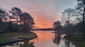 Um lago calmo ao pôr do sol, com árvores e um píer.