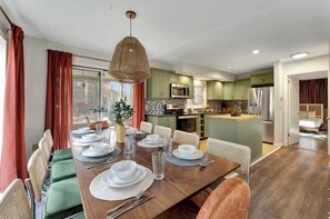 A modern kitchen with green cabinets, a central island, and a dining area with a wooden table set for four.